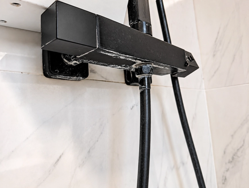 Heavy white limescale around a black shower valve in a hard-water home